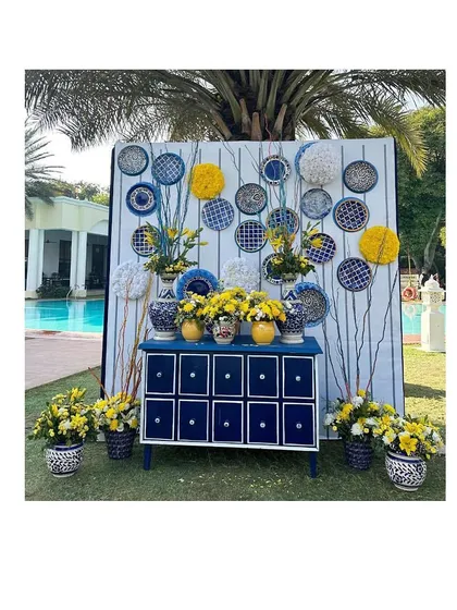 An elegant photo booth we designed for a Blue Pottery themed Haldi. The setup included a custom-painted chest of drawers, floral arrangements, and decorative plates.