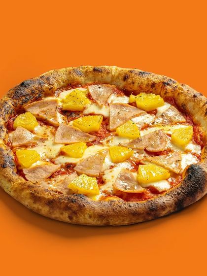 A ham and pineapple pizza with a perfectly charred crust, shot against a solid orange background.
