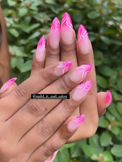 A vibrant pink ombre on stiletto nails, featuring intricate white abstract swirl patterns. This design is both bold in color and delicate in its line work.