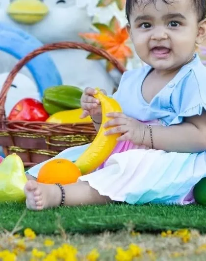 A happy baby girl enjoying some healthy snacks during her birthday picnic.