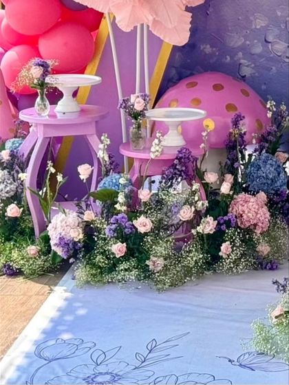 A close-up of the dessert tables and floral arrangements at the base of the backdrop. The scene is filled with details, including small mushroom props and scattered baby's breath.