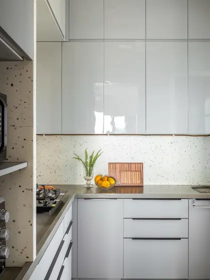 The kitchen is sleek and modern, with glossy white cabinets and a terrazzo backsplash and countertop. This design choice keeps the space bright and clean while adding a touch of playful pattern.