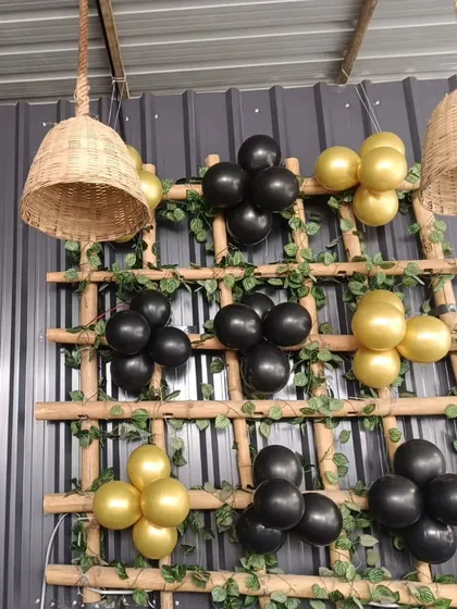 A rustic-chic decoration using a wooden ladder adorned with black and gold balloon clusters and ivy.
