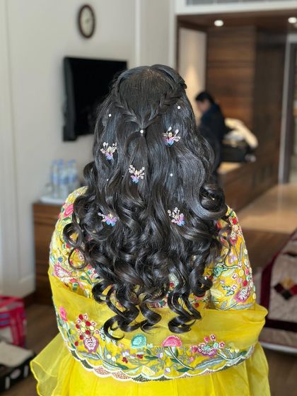 A fun and festive haldi hairstyle with tight curls, braids, and colorful butterfly accessories.