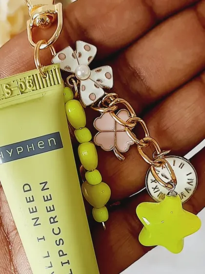 A close-up of a custom lip balm charm in sunny yellow. It features a star, a four-leaf clover, and a clock charm, all handpicked to create a unique piece.