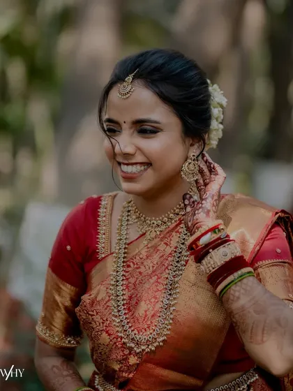 A close-up of this beautiful bride's happy expression. Her makeup features defined eyes and a warm lip color, perfect for her red and gold silk saree.