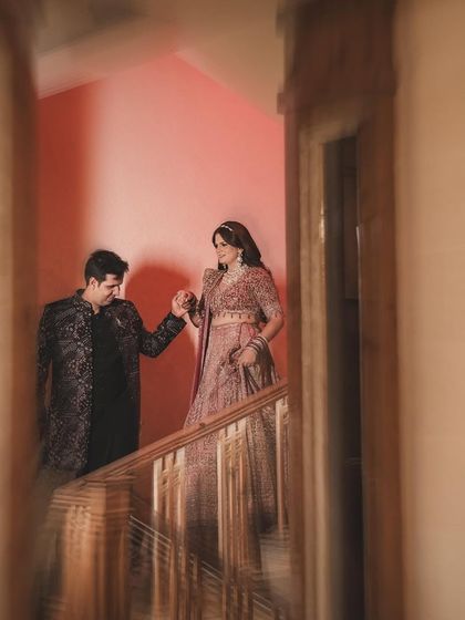 A creative shot through a doorway, capturing the groom leading his bride down the stairs. The unique framing and warm lighting add a narrative quality to this romantic moment.