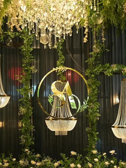 A close-up of the reception decor, showing hanging crystal chandeliers and a custom gold monogram of the couple's initials, framed by fresh greenery. These personalized details make the event unique.