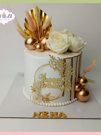 Golden elegance for Neha's birthday. This white cake is adorned with a gold drip, fresh white roses, and a spray of dried botanicals for a boho-chic look.