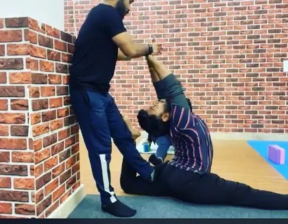 An instructor helps a student deepen their Eka Pada Rajakapotasana (One-Legged King Pigeon Pose), ensuring the backbend is safe and effective.