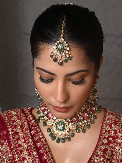 A frontal view focusing on the choker and maang tikka from the same set. The green enamel and Kundan work create a striking contrast against the red lehenga.