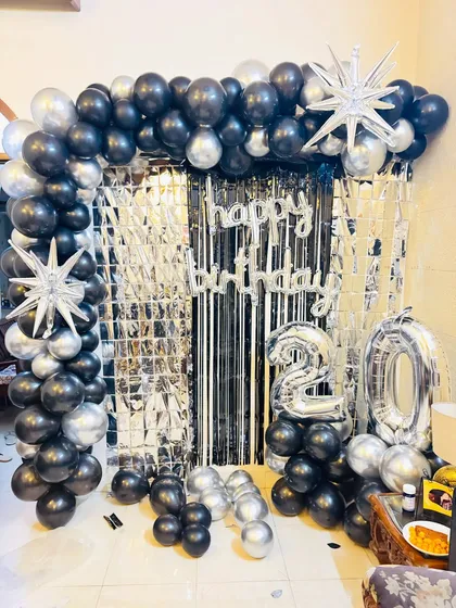 A striking 20th birthday backdrop in black and silver, with a full balloon arch, tinsel curtain, and large star-shaped foil balloons.