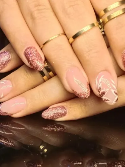 A beautiful rose gold glitter manicure with accent nails featuring delicate white leaf patterns.