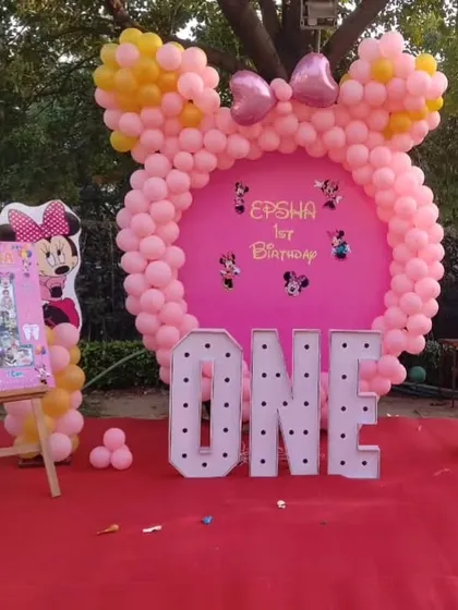 A clear look at our popular Minnie Mouse first birthday theme. This decoration includes a custom pink backdrop shaped like Minnie's head, large light-up 'ONE' letters, character cutouts, and a personalized milestone board for Epsha's special day.