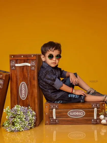 This cool three-year-old is ready to travel, posing with 'Dream' suitcases for his birthday shoot. The yellow background and fun props make for a vibrant and imaginative portrait.