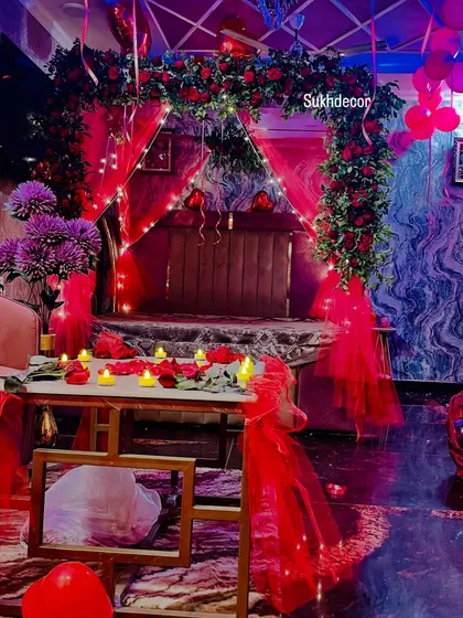 This perspective shows the entire romantic scene from a lower angle, highlighting the candlelit table with rose petals and the glowing bed canopy in the background.