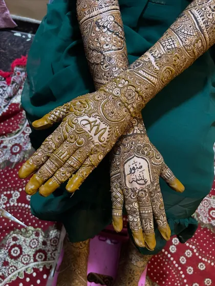 A crossed-hands pose showing both names beautifully displayed on the palms, surrounded by intricate mehendi patterns.