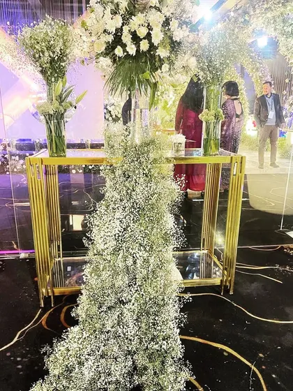 A modern and elegant console table arrangement for an engagement party, featuring tall glass vases with baby's breath and a cascade of florals down the side.