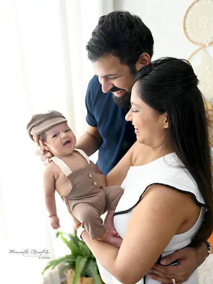 A playful moment with a newborn. The parents hold up their smiling baby, who is dressed in an adorable outfit with a matching cap, showcasing his happy personality.