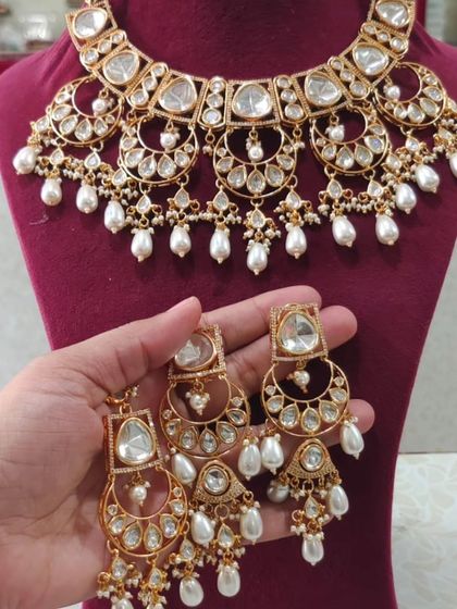 A gold-plated Kundan necklace set with a unique chandbali design and pearl drops.