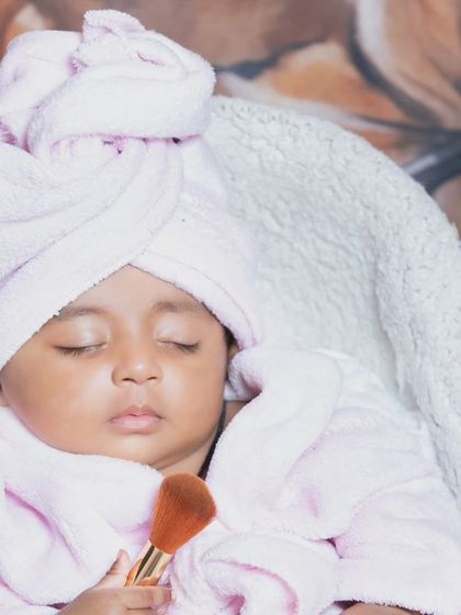 A close-up of the sleeping baby in her bathrobe, holding a makeup brush.