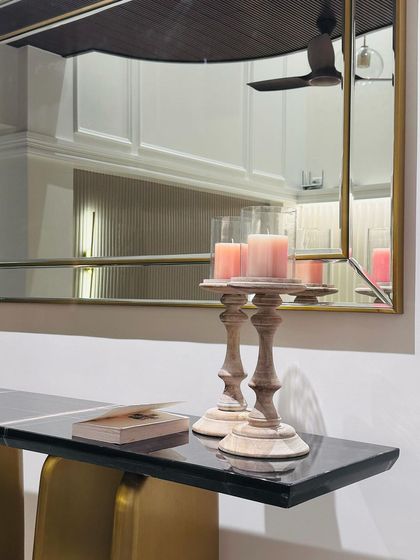 A close-up of the foyer console table, showing the rich black marble top styled with wooden candle holders. The vintage mirror reflects the space, adding depth and light.