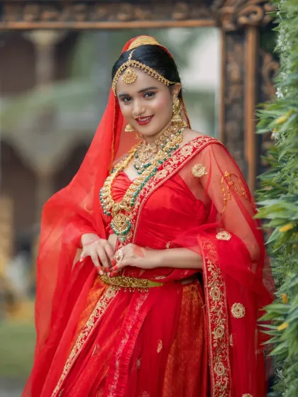 A classic North Indian bridal look in a vibrant red lehenga. The makeup is glamorous with defined eyes, and the look is completed with a maang tikka and nath.
