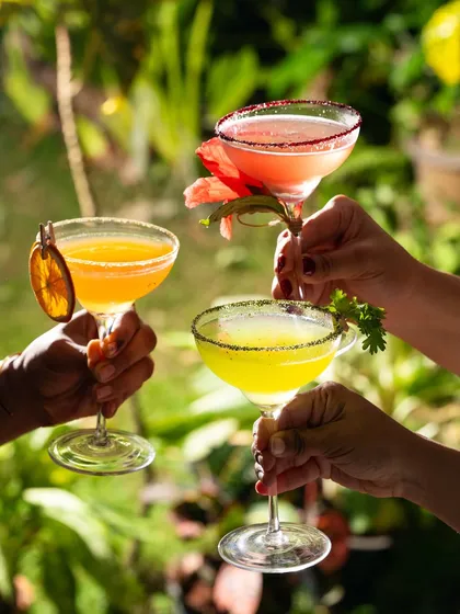 Three colorful cocktails raised for a toast. This image is all about celebration, friendship, and the social aspect of drinking.