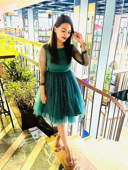 Pooja looks gorgeous in this custom-made emerald green party dress. The design features sheer sleeves and a layered tulle skirt with subtle polka dots, perfect for a birthday or cocktail event.