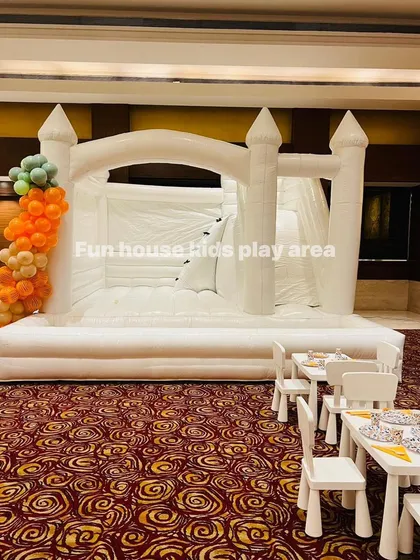 Our 4-in-1 white bouncy castle stands impressively next to our kids' table and chair setup. This inflatable includes a jumping area, slide, climbing wall, and ball pit for maximum fun.