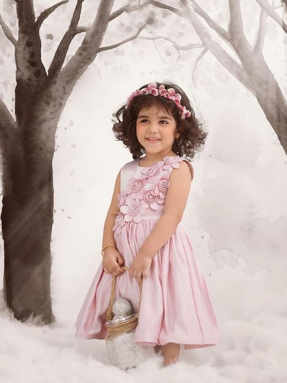 A painterly style portrait featuring a little girl in a pink dress against a watercolor-style winter forest backdrop. This artistic approach creates a unique, storybook feel.