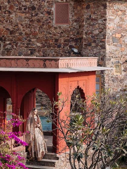 A bride stands on a balcony of the fort, the red stone and pink bougainvillea complementing her outfit.