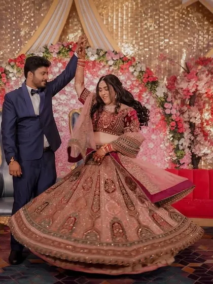 A fairytale twirl during the Sangeet. The groom leads his bride in a dance, her magnificent lehenga spinning around her against a backdrop of lush pink florals.