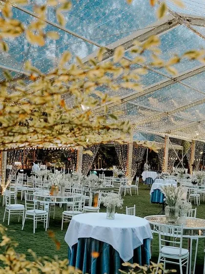 The clear-top tent seen from outside, glowing against the evening sky. This image captures the magical ambiance we create for our sangeet celebrations.