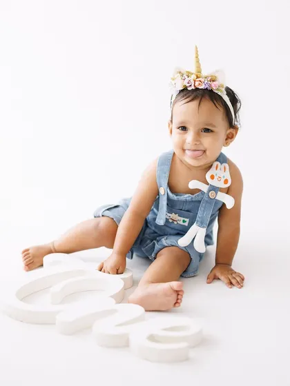 A playful moment from her first birthday shoot. Her sweet expression and adorable unicorn-themed outfit make for a truly memorable and cute milestone portrait.
