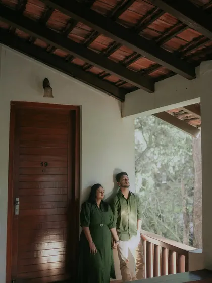 A beautifully composed shot using the architecture of the resort. The couple stands on a balcony, framed by the wooden beams, looking out towards their future.