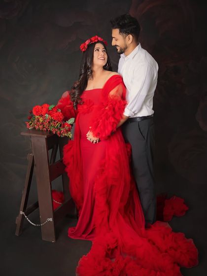 The look of love between expecting parents. This portrait captures the sweet connection and excitement as they await their little one, surrounded by beautiful red floral props.