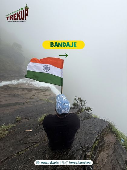 A trekker sits at the edge of a cliff at Bandaje, holding the Indian flag as it billows in the wind.