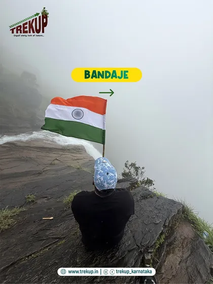 A trekker sits at the edge of Bandaje falls, holding the Indian flag. This spot offers a dizzying view straight down the 200-ft drop, a truly humbling experience.