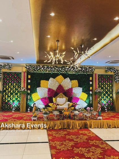A grand Seemantham stage in a modern hall, featuring a large, multi-colored floral lotus as the centerpiece. This design beautifully blends traditional artistry with a contemporary setting.