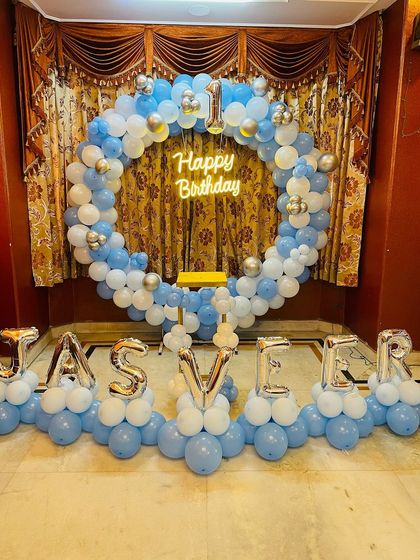 A personalized birthday setup with a large balloon ring and name balloons. The name "JASVEER" is spelled out in silver foil letters in front of the blue and white ring.