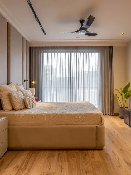 A serene bedroom design from one of my builder floor projects. The room features a padded fabric headboard, wooden flooring, and large windows with sheer curtains to create a warm, light-filled, and minimalist space.