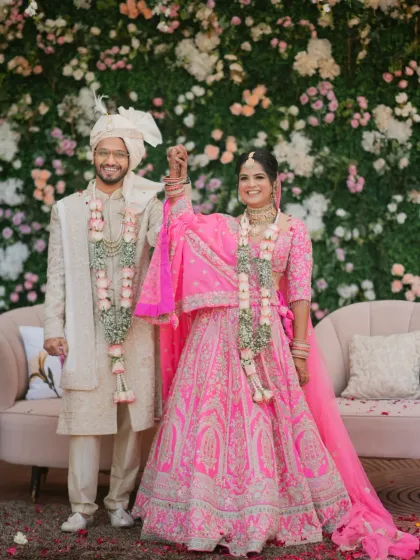 A joyous portrait of the couple after their varmala exchange, standing in front of a beautiful floral wall.