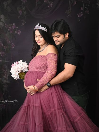 A royal-themed couple's portrait. The mom-to-be wears a tiara and holds a bouquet, while her partner embraces her lovingly in this elegant shot.