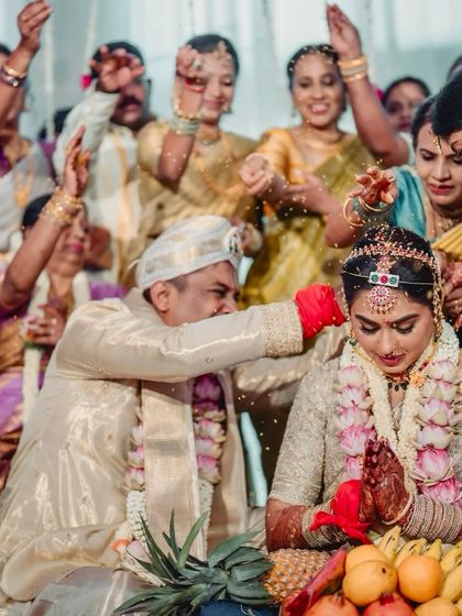 A candid moment from a wedding ceremony. The bride and groom are dressed in matching cream and gold traditional attire, designed to look cohesive and elegant during the rituals.