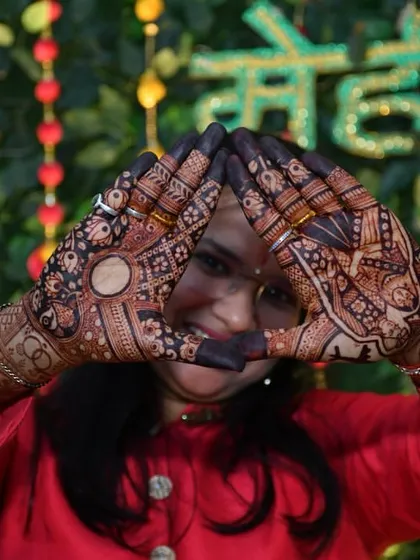 A fun pose framing the face with beautifully stained hands. The contrast between the dark henna and the skin is what makes a great mehendi design truly pop.
