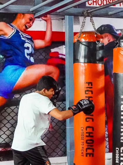 A young member practices his boxing combinations on the heavy bag. Behind him, the wall art shows the energy and power we inspire in all our fighters. Fitness, fun, and fighting, that's what we are about.