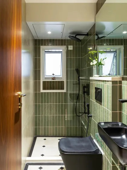 This bathroom uses earthy green vertical tiles to create a calming, spa-like feel. The black fixtures and patterned floor tiles add a touch of modern contrast and personality.