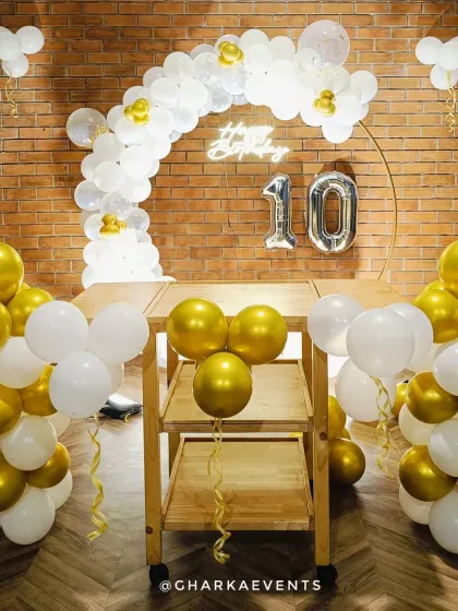 A classic 10th birthday celebration in gold and white. The simple setup with a balloon arch over a bar cart is perfect for a stylish and intimate gathering.