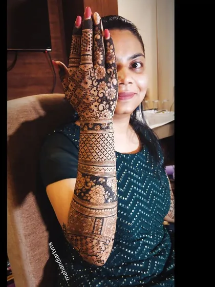 A client posing with her intricate full-arm mehandi. The design uses a mix of floral bands and geometric fillers for a balanced look.